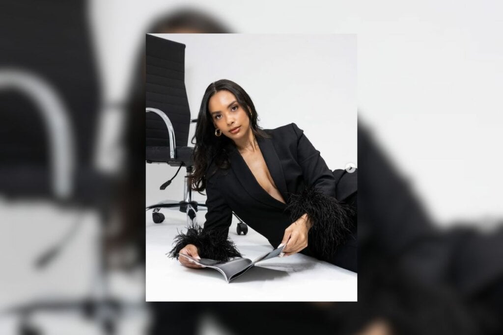 Mulher com cabelo castanho escuro longo, usando um blazer e deitada de lado em um fundo branco 