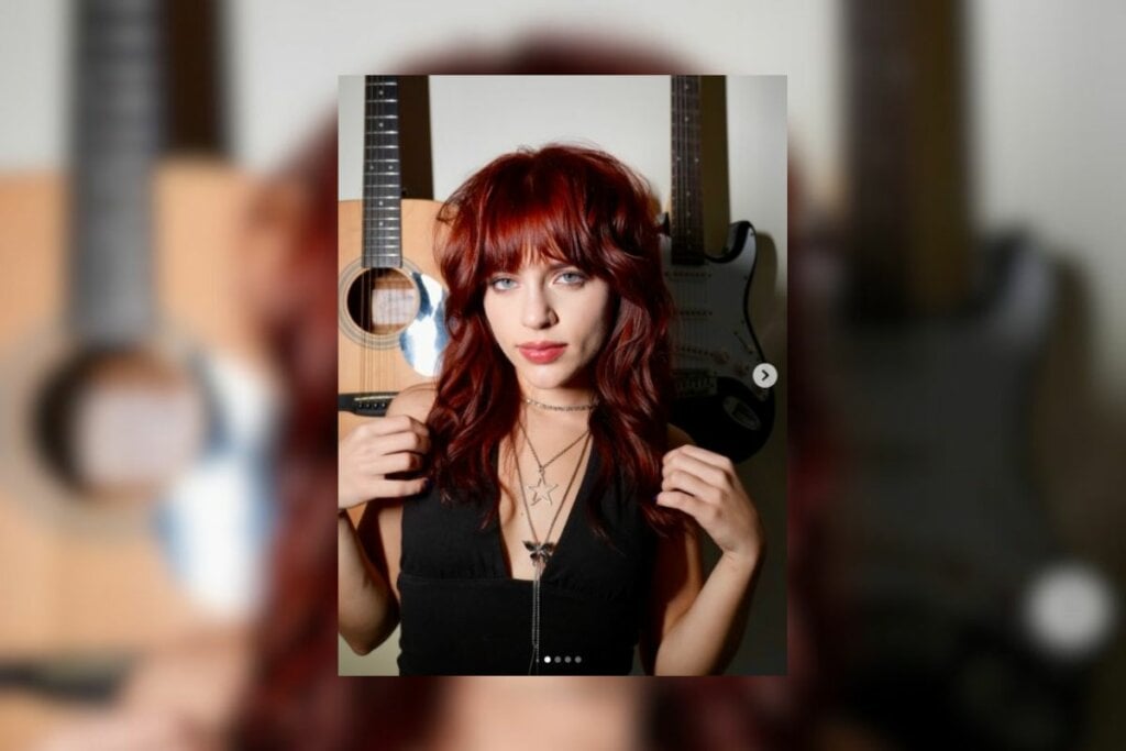 Mulher com cabelo ruivo com franja e usando uma blusa preta posando para foto 