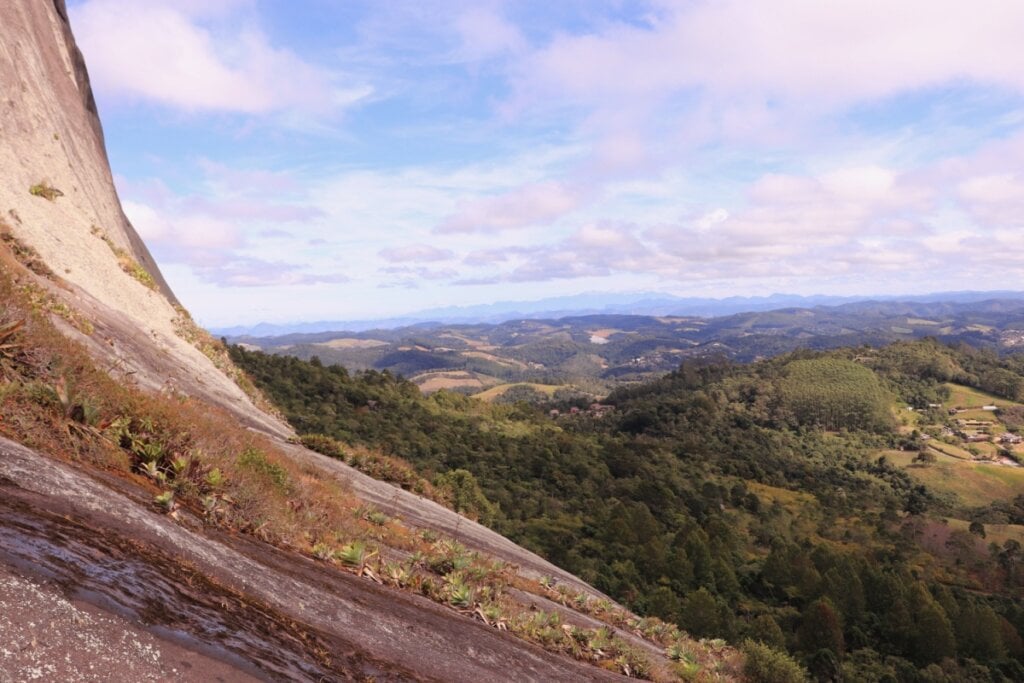 Vista da Serra Capixaba com uma montanha na frente e, ao fundo, uma paisagem verde. Acima um céu-azul com nuvens brancas 